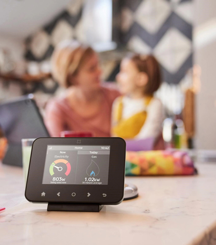 Image Of A Smart Meter In The Foreground With A Mother And Child Sitting In The Background